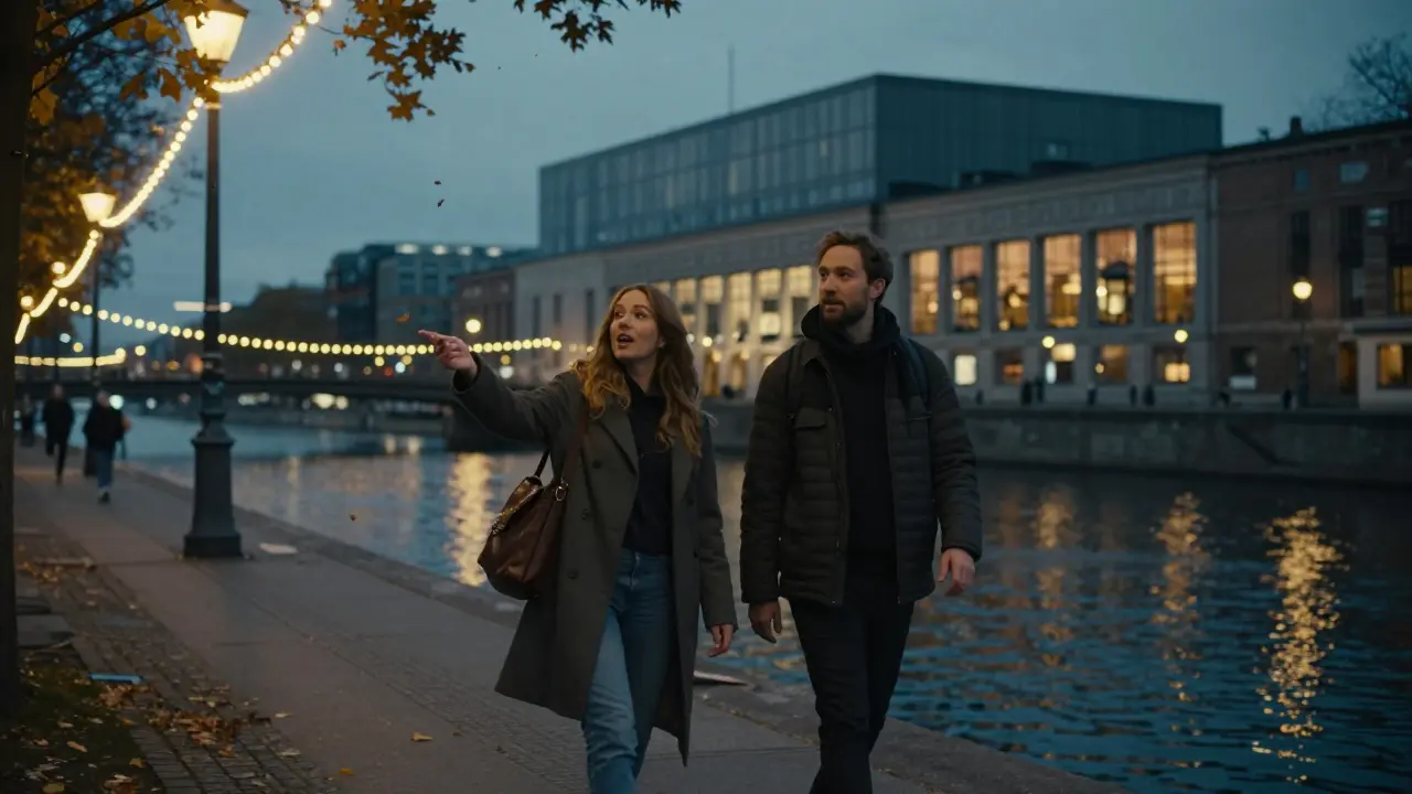 Two people walking along the Spree River at dusk, admiring the Hamburger Bahnhof museum with quiet mutual interest.